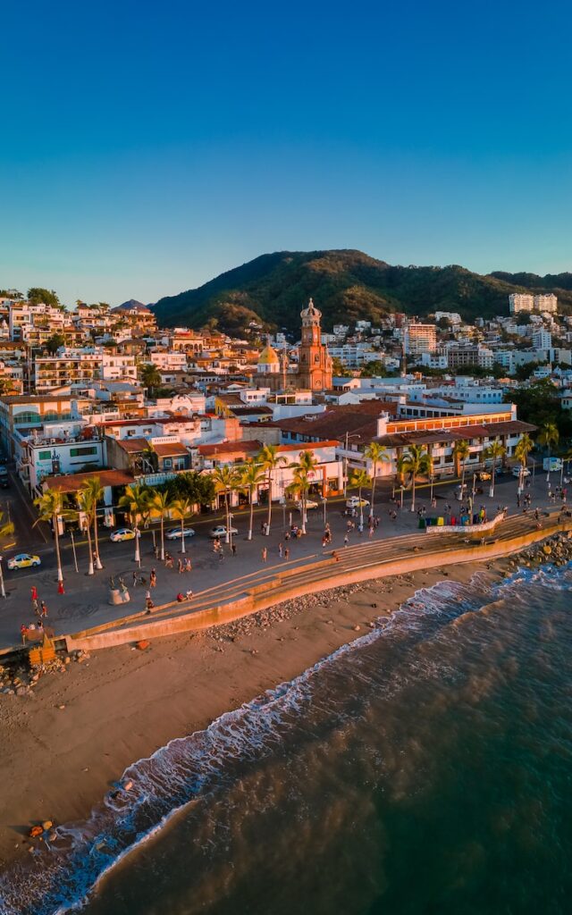 People walk along the beach at sunset at a beach town with green mountain to the top right