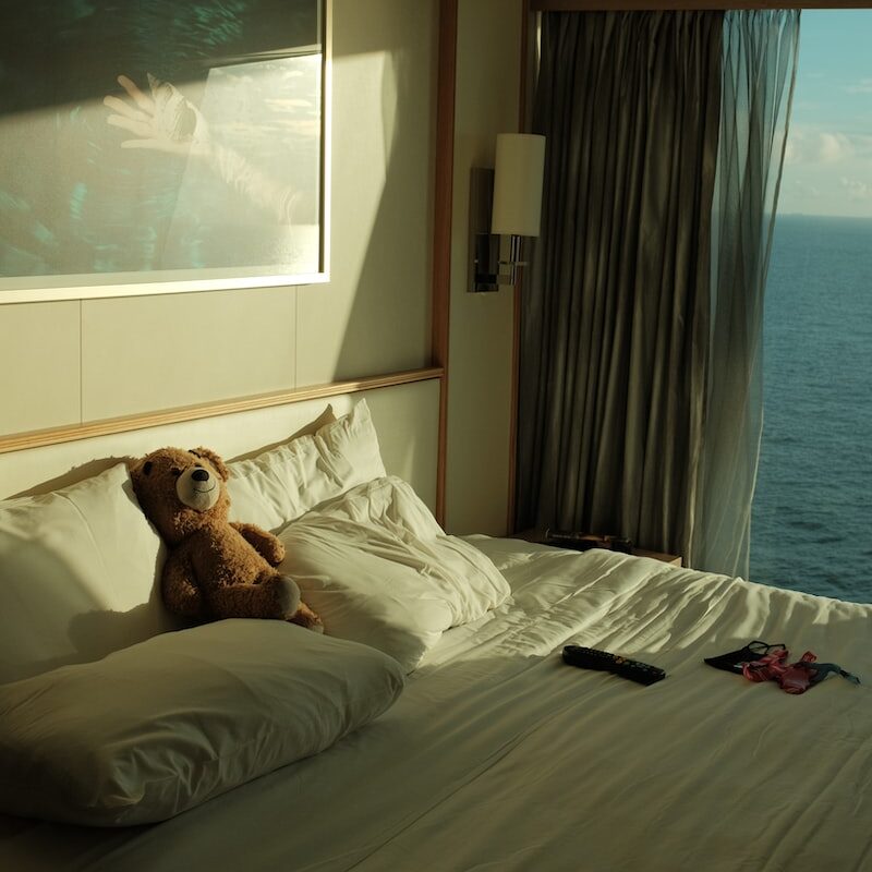 Teddy bear on white bed by ocean-view window