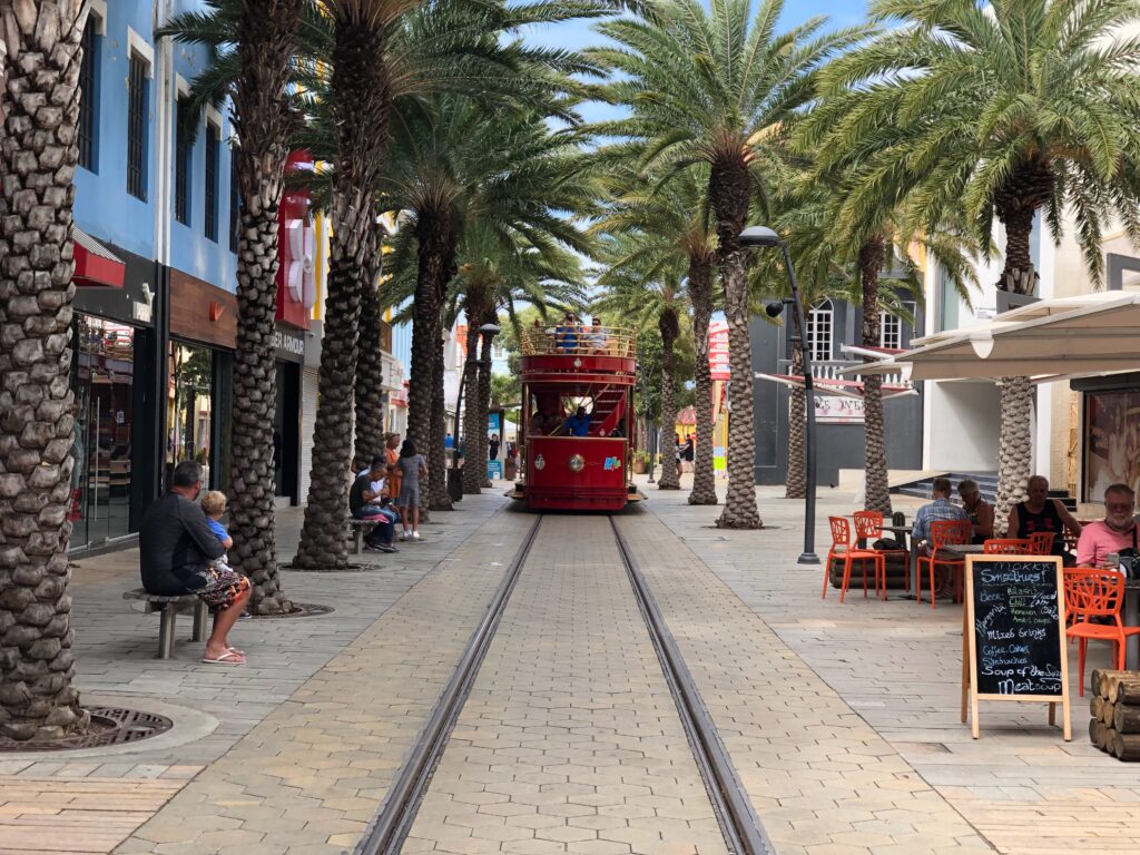 Red trolley car surrounded by storefronts and palm trees