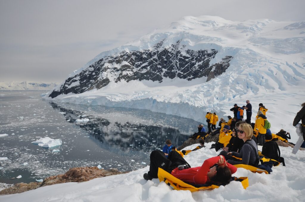 people in red and yellow sit on snow toward body of water