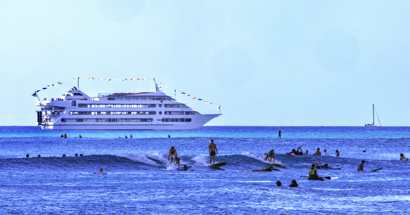 people swimming and surfing as a cruise ship is arriving in Honolulu in the background 