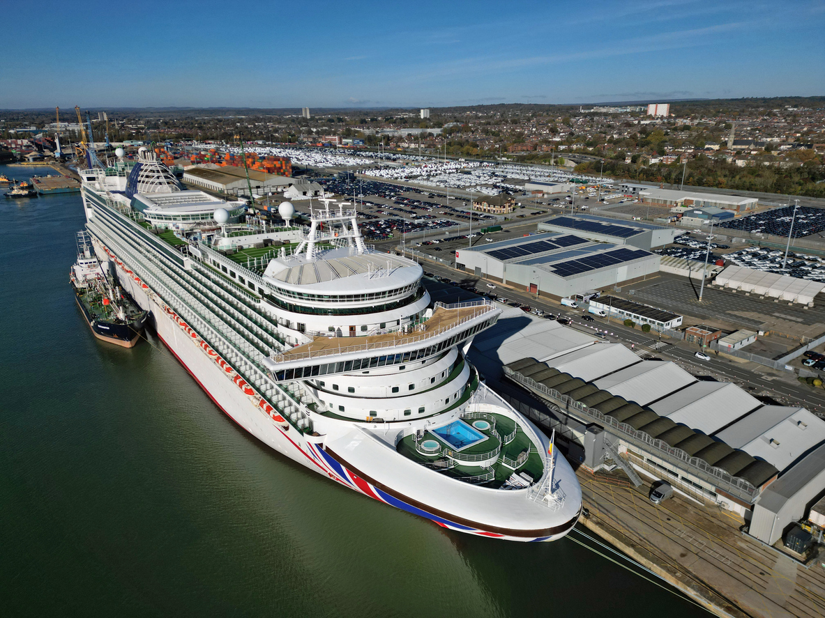 Ventura cruise ship at Southampton Port UK with support boat next to it. Main deck and swimming pool. Wide aerial view of Southampton Docks with car terminal and warehouses