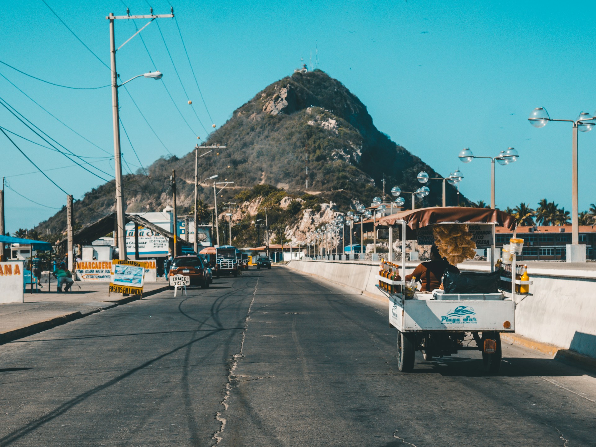 The road in Old Mazatlan. Lots of shacks on the side of the road and a large hill in the background.