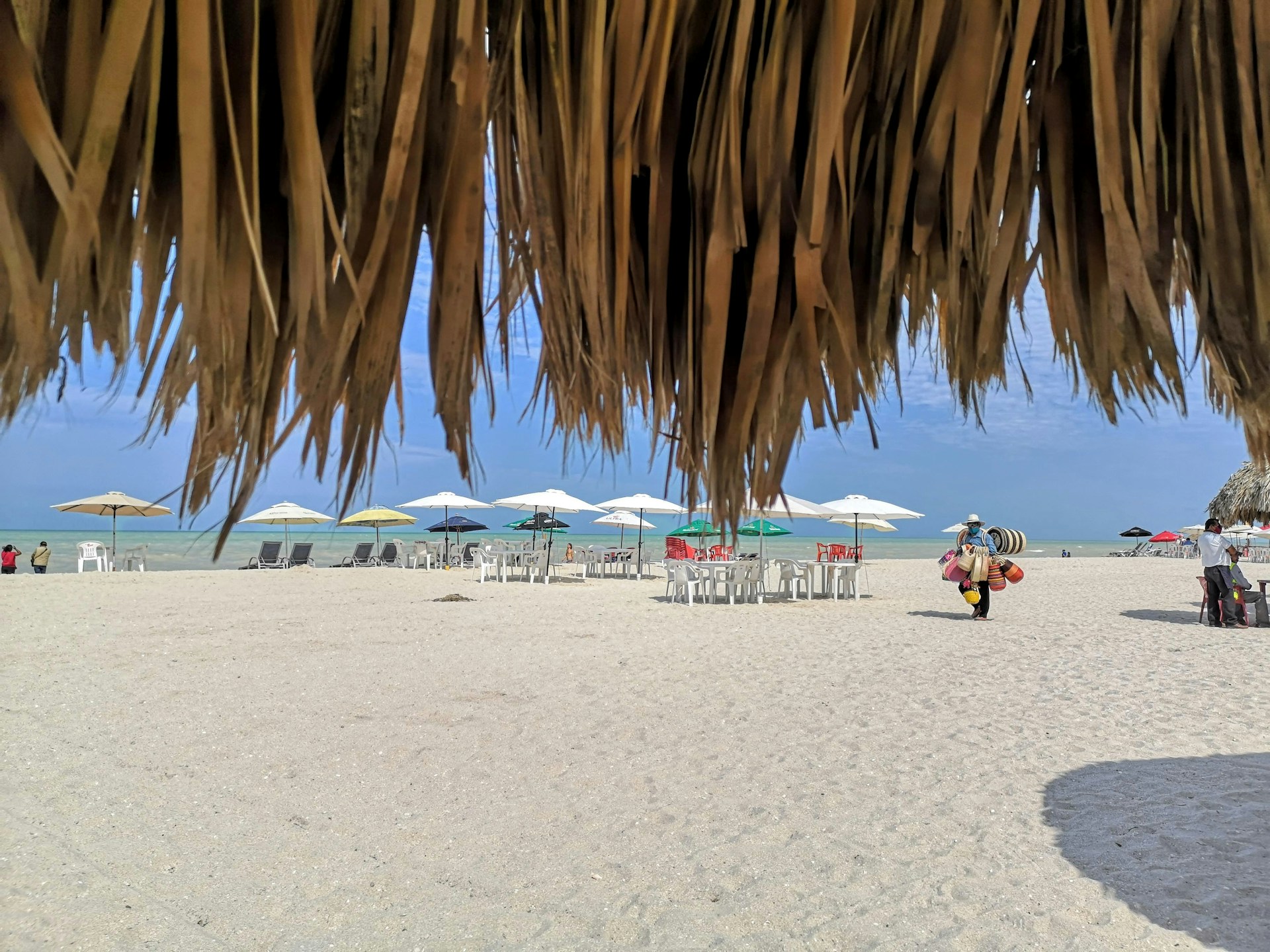 View of the beach from under a tiki hut with umbrellas and chairs facing the ocean in Progreso, Mexico
